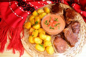 Friptura de porc si cartofi cu unt la cuptor, servite cu sos de usturoi si rosii